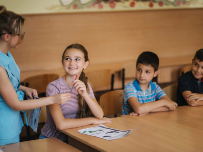woman handing a ballpen to a little girl inside the classroom